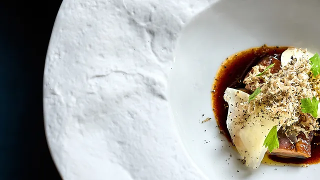Gourmetgericht mit Trüffelspänen, Sauce und Garnitur auf strukturiertem weißen Teller